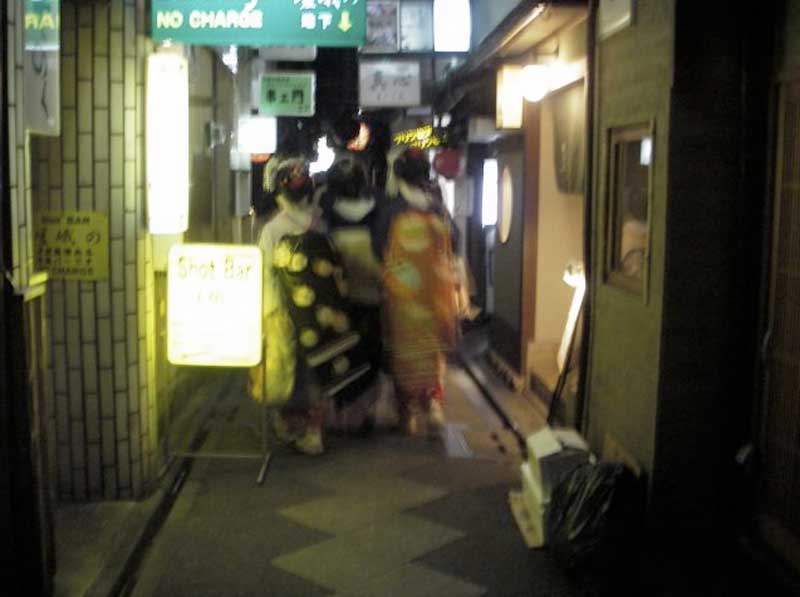 blurry photo of three maikos stumbling down a narrow street