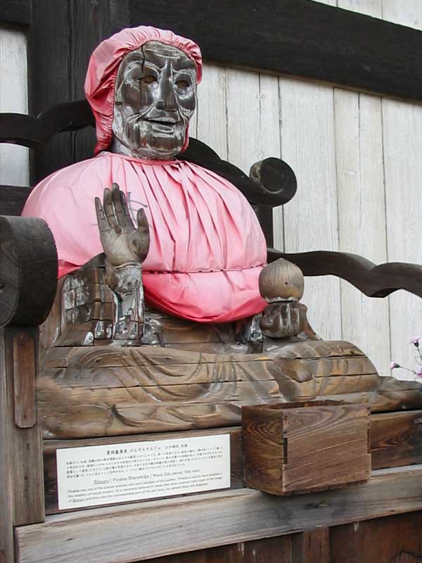 large wooden statue outside temple wearing pink hat and bib