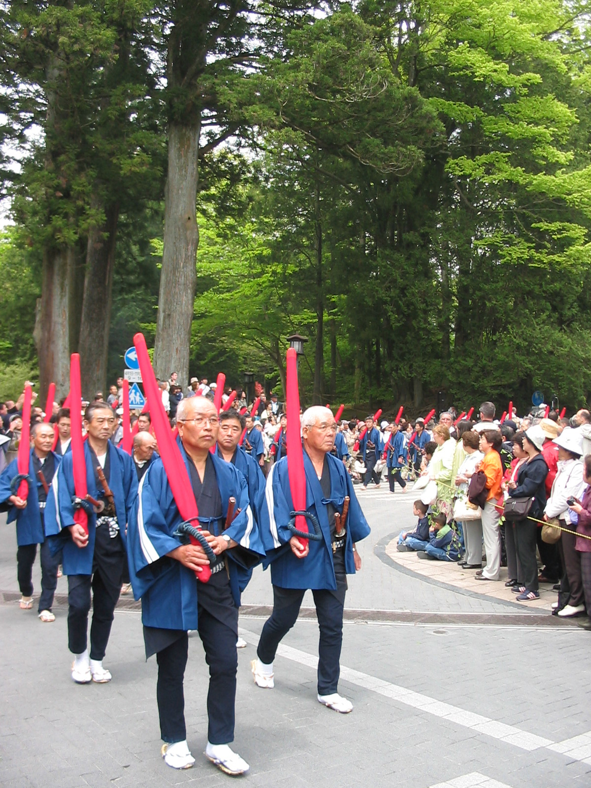 men in parade in traditional clothing and holding poles in red cloth