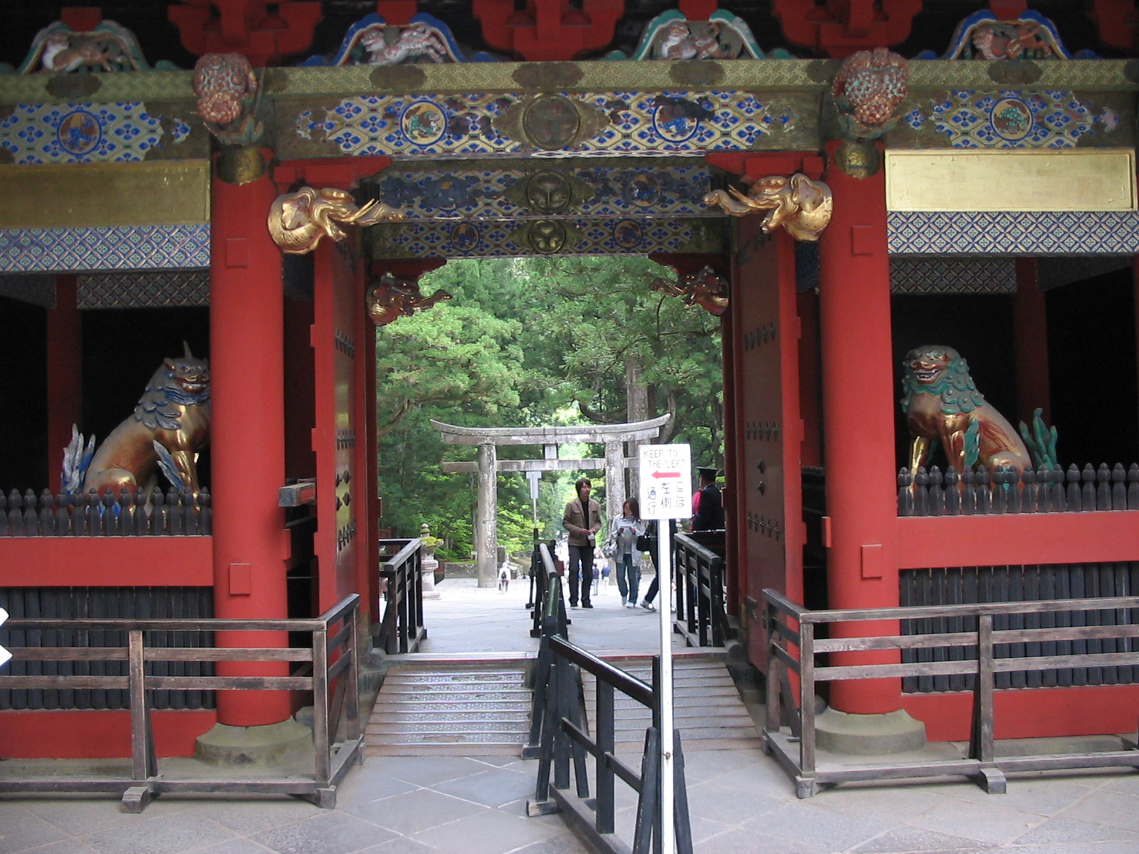 red wooden gate with decorations and view of stone torri gate through entrance